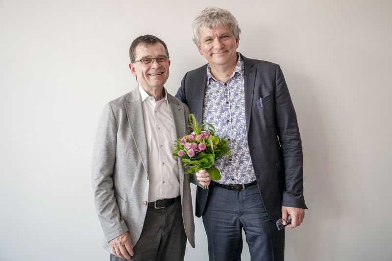 Zwei Herren, Wolfgang Hirschmann und Carsten Lange stehen nebeneinander und blicken in die Kamera, der linke hält einen Blumenstrauß in der Hand