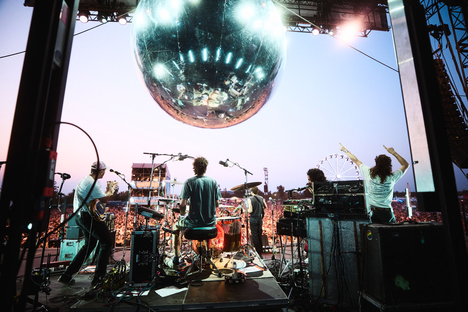 Blick von Backstage auf die Bühne eines Openair Festivals. Im Hintergrund ist zahlreiches Publikum zu sehen