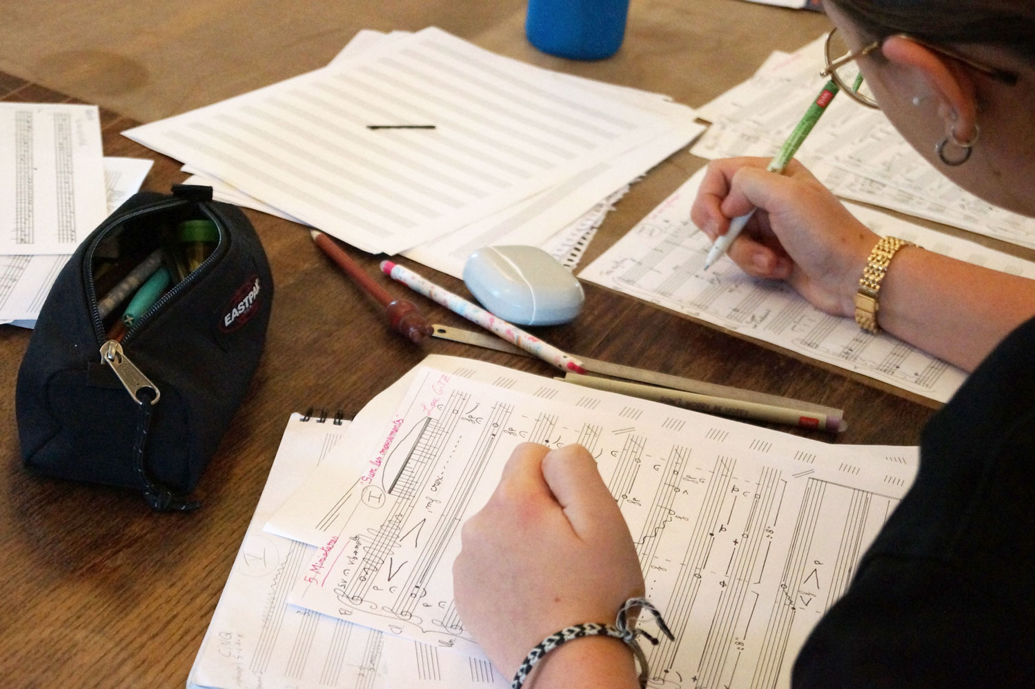 Notenblätter liegen auf einem Tisch – darüber zwei Hände, eine davon hält einen Stift