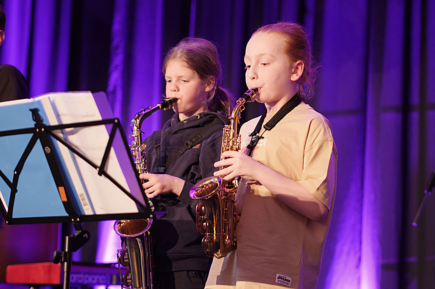 Zwei Kinder stehen mit ihren Sxophonen musizierend auf einer farbig beleuchteten Bühne